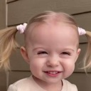 Toddler with pigtails giving a squinty, mischievous grin.