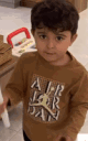 A young boy in a brown shirt stares directly at the camera with a serious and focused expression.