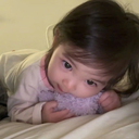 A toddler resting their head on a purple plush toy with a soft, curious expression.
