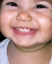 Toddler with a wide, mischievous, toothy grin looking directly at the camera.