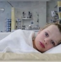 A young child lying in a hospital bed looking directly at the camera with a tired expression.