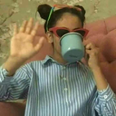 Person wearing red sunglasses and holding a hand up while sipping from a blue mug.