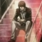 Light Yagami sitting on stairs with a serious and calculating expression.