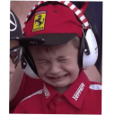 A young boy wearing a red racing cap and large white noise-canceling headphones, crying with his eyes squeezed shut.