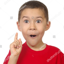 A young boy in a red shirt with a shocked expression pointing his index finger upward.