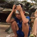 A young boy crouching while holding his head in his hands with an expression of pain.