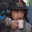 Man wearing a PlayStation cap and headphones sips from a small white cup with a focused expression.