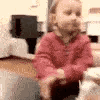 A toddler wearing a red sweater looks around with a skeptical and unimpressed facial expression.