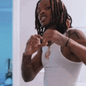 King Von making a heart shape with his hands while wearing a white tank top and gold chain.
