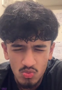 Young man with dark curly hair making a puckered lip expression of confusion.