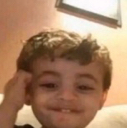 A young child with messy hair wearing a mischievous, slightly smug grin.