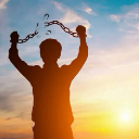 Person in silhouette breaking chains against a bright sunrise background.