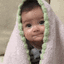 Baby wrapped in a purple blanket with a green trim slowly transitioning into a wide, happy smile.