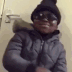 A young child wearing sunglasses and a winter hat makes a shushing gesture with their finger.