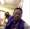 Young man wearing glasses and a purple jacket holding his fist up in an aggressive gesture.