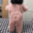 A toddler in a pink onesie dancing rhythmically on a checkered surface.