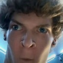 A man with curly hair looking directly into the camera with a wide-eyed, confused expression.