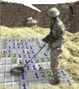 Soldier in uniform scanning a giant Minesweeper grid with a metal detector.