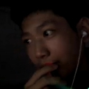Person with wide eyes and a hand near their mouth looking suspicious in low light.