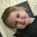 A young child with brown hair tilting their head and giving a playful, knowing smirk.
