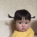 A toddler with pigtails stares directly at the camera with a deadpan, judgmental expression.