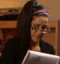 Bayley wearing glasses and a headband looking down at a notepad while writing.