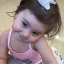 A young girl with a white bow in her hair tilts her head with a playful expression.