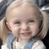 A young girl with pigtails giving a mischievous, knowing grin.