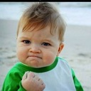 Toddler clenching a fist in a gesture of success while on a beach.