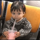 A toddler with a suspicious expression holding a pink drink with a straw.