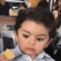 A toddler looking to the side with a skeptical expression while holding a piece of food.