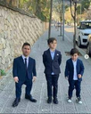 A man and two children standing on a sidewalk wearing matching navy blue suits.