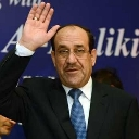 Nouri al-Maliki waving his hand in a formal suit and tie.