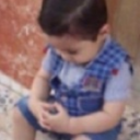 A young boy with dark hair looking down with a pensive expression.