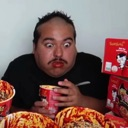 A man looking shocked with wide eyes while holding a cup of noodles.