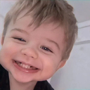 A toddler with light brown hair smiling broadly with a joyful expression.