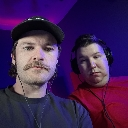 Two men wearing headsets staring directly into the camera with intense, menacing expressions under purple lighting.