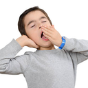 Young boy yawning with his hand over his mouth and eyes closed.