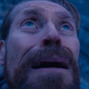 Willem Dafoe looking upward with a wide-eyed, distressed expression in a blue-toned lighting.