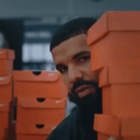 Drake peeking from behind a stack of orange shoeboxes with a suspicious look.