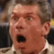 Vince McMahon looking shocked and falling backwards out of an office chair in a wrestling ring.