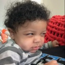 Baby with curly hair looking sideways with a skeptical and judgmental expression.