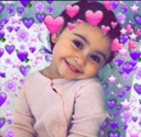 A young child smiling shyly with a filter of pink and purple hearts floating around their head.