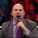 Adam Pearce shouting intensely into a microphone with a red background.