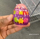 A hand holding a small purple plastic egg toy with bunny characters printed on it.