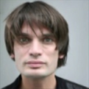 Man with a bowl cut looking directly at the camera with a neutral, unamused expression.