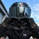 Motorcyclist wearing a black helmet and gloves making a heart shape with their hands.