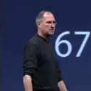 Steve Jobs standing on stage with a serious expression next to a large number 67.