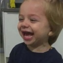 A toddler with blonde hair laughing with their mouth wide open.
