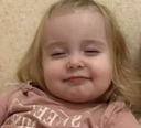 Toddler with blonde hair giving a smug, knowing smirk.